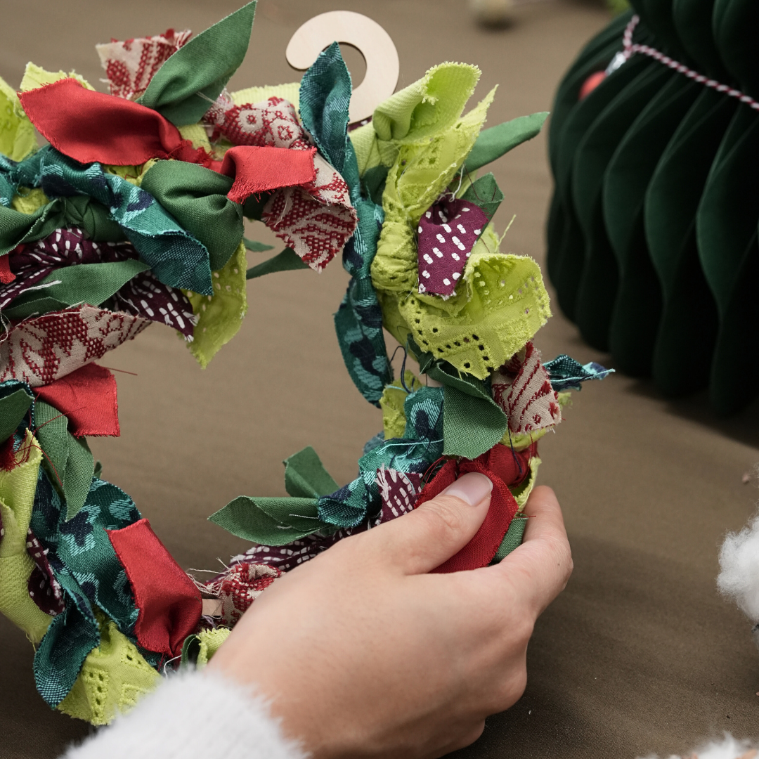 Hand holding a colorful fabric wreath with a blurred background