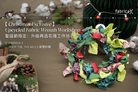 Colorful upcycled fabric wreath with Christmas decorations on a brown surface, hosted by 'Fabrica X'.