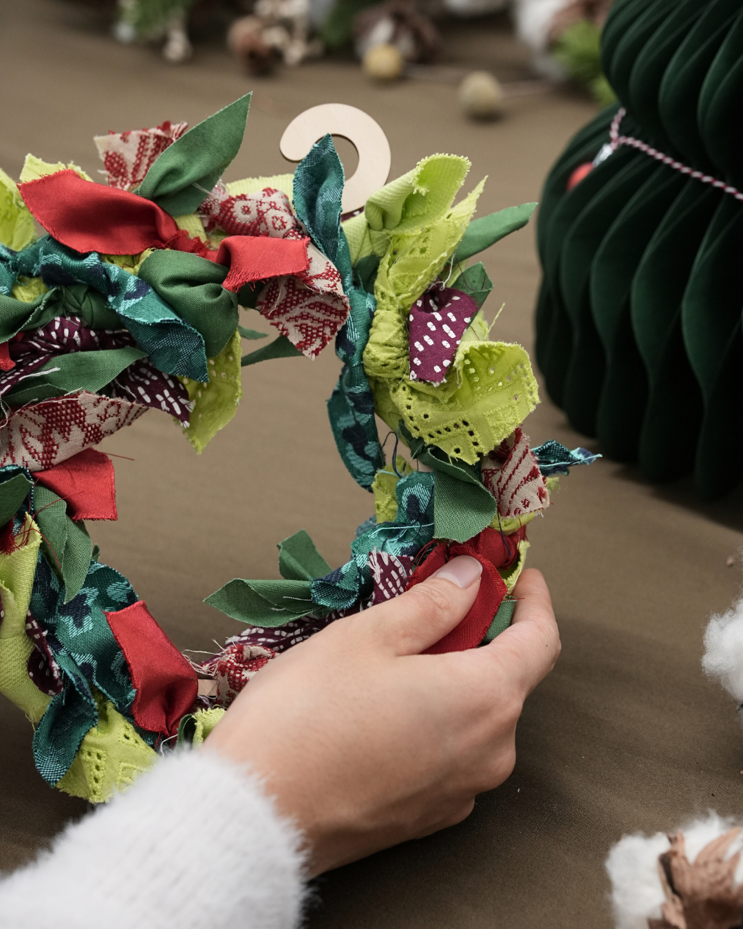 Hand holding a colorful fabric wreath with a blurred background